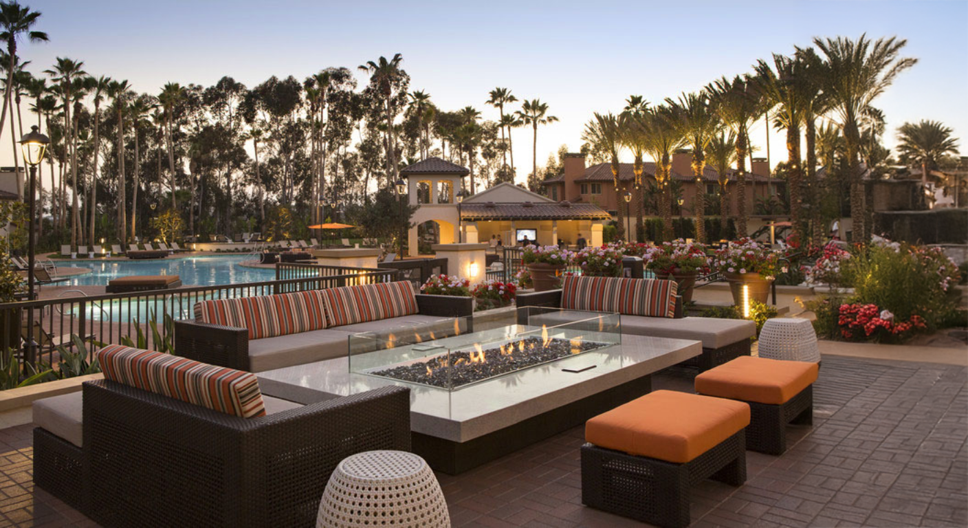 Outdoor patio area with fire pit, lounge chairs, and palm trees at dusk.
